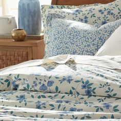 an unmade bed with blue and white flowers on the comforter, next to a nightstand