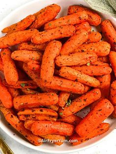 a white bowl filled with cooked carrots on top of a table next to a fork