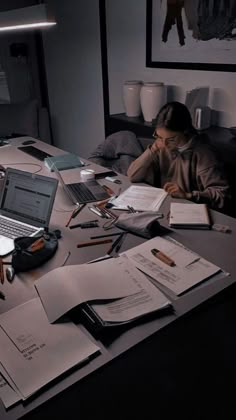 a man sitting at a desk with several papers and laptops on top of it