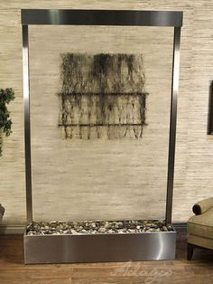 a wall mounted fountain with rocks and pebbles in the bottom, on a wooden floor