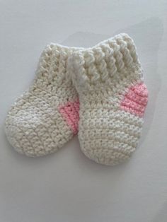 two white knitted baby shoes with pink accents