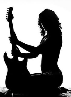 a woman sitting on the ground with a guitar in her hand and she is playing