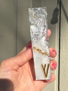 a person holding up a piece of foil with the letter v on it's side