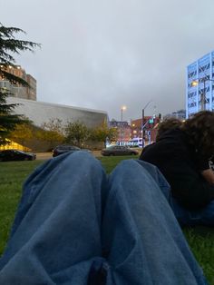 a person laying on the grass with their feet up in the air and buildings behind them