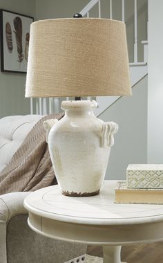 a white vase sitting on top of a table next to a lamp and chair in a living room