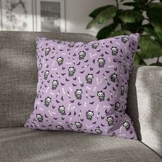 a purple pillow with skulls and bones on it sitting on a couch next to a potted plant