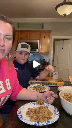 two people sitting at a table with plates of food in front of them and one person holding a spoon