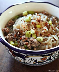 a close up of a bowl of food with noodles and meat in it on a table