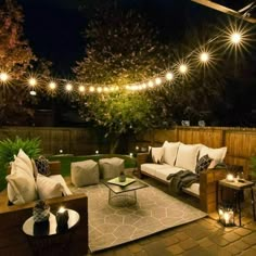 an outdoor living area with couches, tables and lights on the side of it