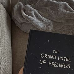 a book sitting on top of a couch next to a pillow and blanket with the words grand hotel of feelings written on it