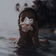 a woman floating in the water holding a flower up to her face