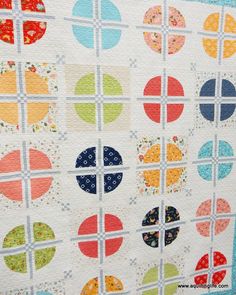 a quilt made with circles and squares on the side of a white wall hanging in front of a window