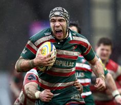 a rugby player with his mouth open and holding the ball in one hand, while other players run behind him