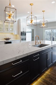 a large kitchen with marble counter tops and gold pendant lights hanging from the ceiling over the sink