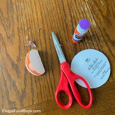 a pair of red scissors sitting on top of a wooden table next to some crafting supplies