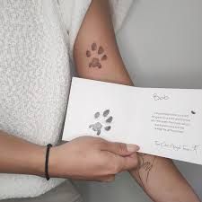 a person holding a piece of paper with a dog paw tattoo on it's arm