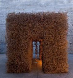 a sculpture made out of straw sitting on top of a cement floor next to a brick wall