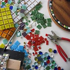 the table is covered with many different colored glass tiles and tools for making mosaics