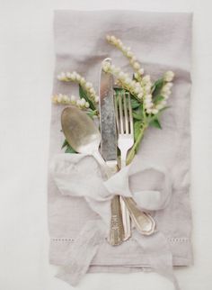 two forks and spoons sitting on top of a napkin with white flowers in it