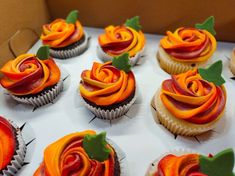 cupcakes decorated with orange and red icing in a box on a table