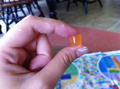 a person is holding an orange pill in their left hand while sitting at a table