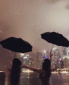 two people holding umbrellas in front of a cityscape at night with rain falling on them