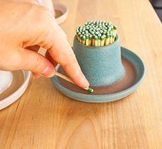 a person is holding a match stick in a small cup on a wooden table next to a plate