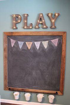 a chalkboard with lights on it and some buckets in front of it that says play