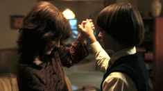 two young children standing next to each other in a living room, one holding the hand of another child's head