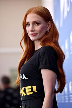 a woman with long red hair wearing a black t - shirt