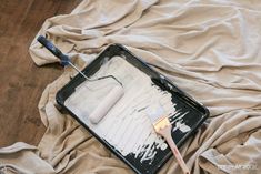 a tray with paint and a brush sitting on top of a bed covered in sheets