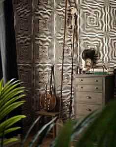 a room with a dresser, chair and wallpaper on the walls that has black and white designs