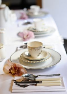 the table is set with silver and white dishes, cups, and saucers on it