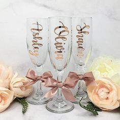 three wine glasses with the word bride written on them and pink flowers in front of them