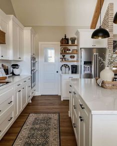 a large kitchen with white cabinets and wooden flooring, an area rug in the middle