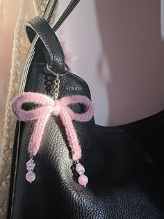 a black purse with a pink bow on the handle and some beads hanging from it