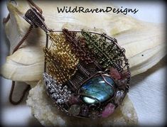 a wire wrapped pendant is sitting on top of a piece of wood and has many different colored stones in it