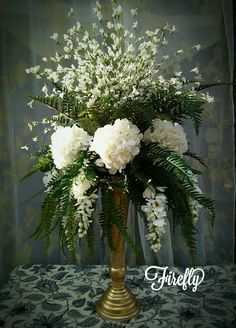 white flowers are in a gold vase on a table