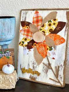 a wooden sign with flowers on it sitting next to a pumpkin and some other decorations