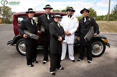 a group of men standing next to each other in front of an old fashioned car