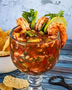 a glass filled with food and garnished with cilantro, limes, and chips