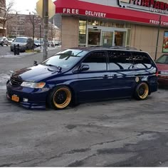 a blue minivan parked in front of a pizza hut with gold rims on it