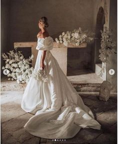 a woman in a white wedding dress standing next to a fireplace