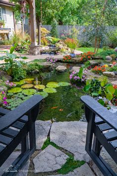 two black benches sitting next to a pond filled with water lilies and other flowers