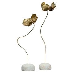 two metal flower sculptures on marble bases with gold leaf tops, set against a white background