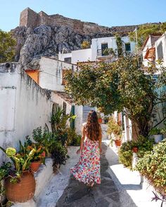 a woman walking down a narrow alley way with potted plants and buildings in the background