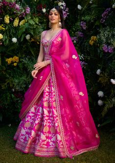 a woman wearing a pink and yellow lehenga with flowers in the back ground