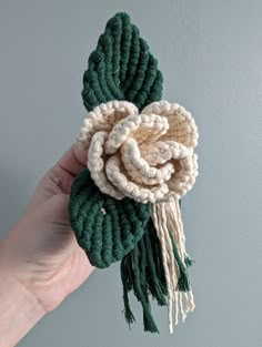 a hand holding a crocheted flower with tassels