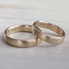 two gold wedding rings sitting on top of a wooden table