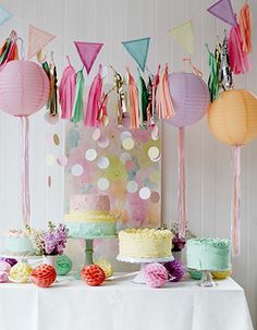 a table topped with lots of cake covered in frosting and paper lanterns hanging from the ceiling